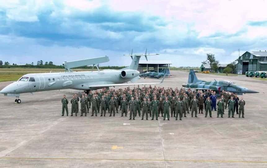 Militares se reúnem na frente do E-99 e F-5EM na Base Aérea de Canoas na abertura do Exercício Escudo-Tínia.